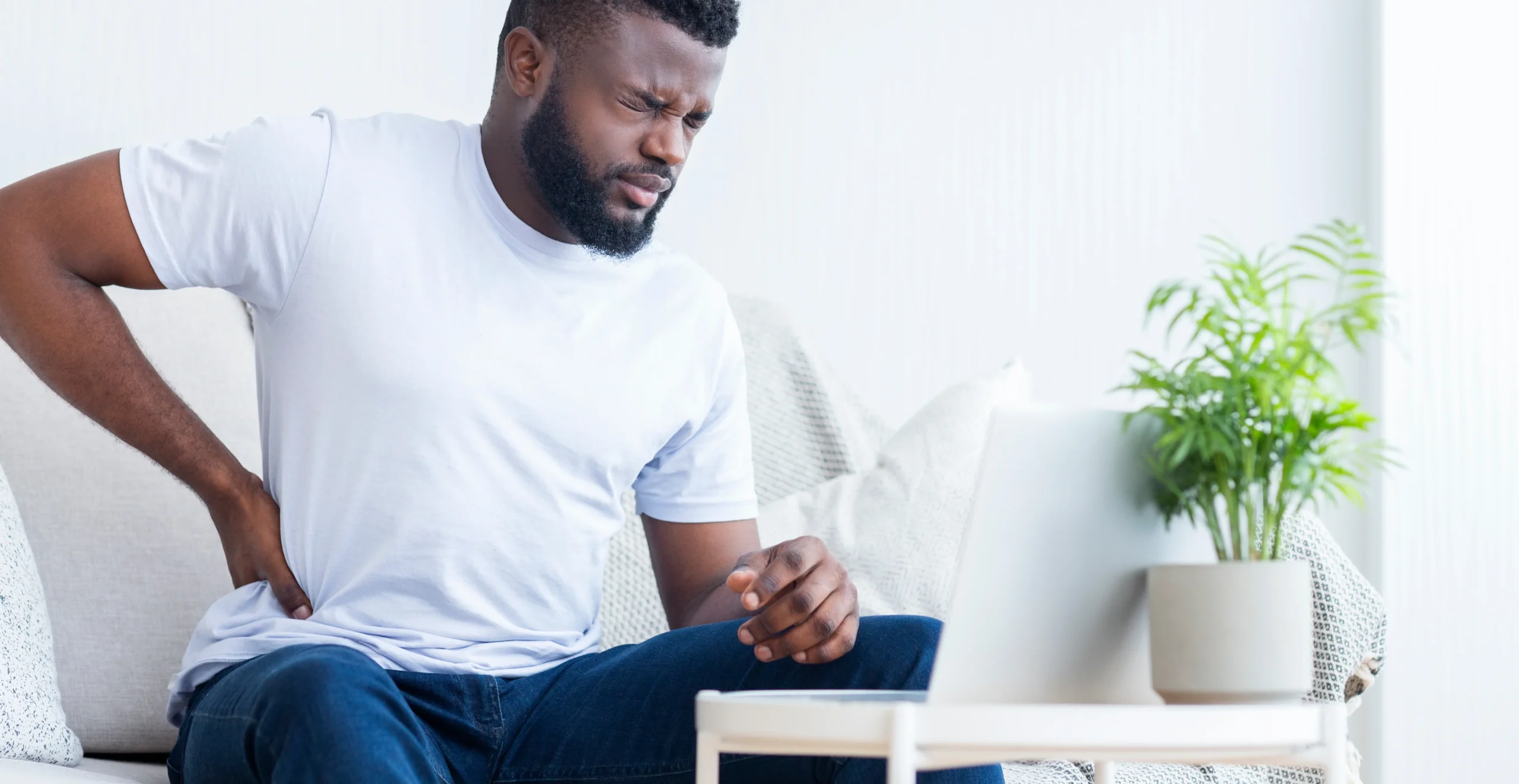 A man is seated on a couch, turned away from the camera, representing the impact of back pain on daily life.
