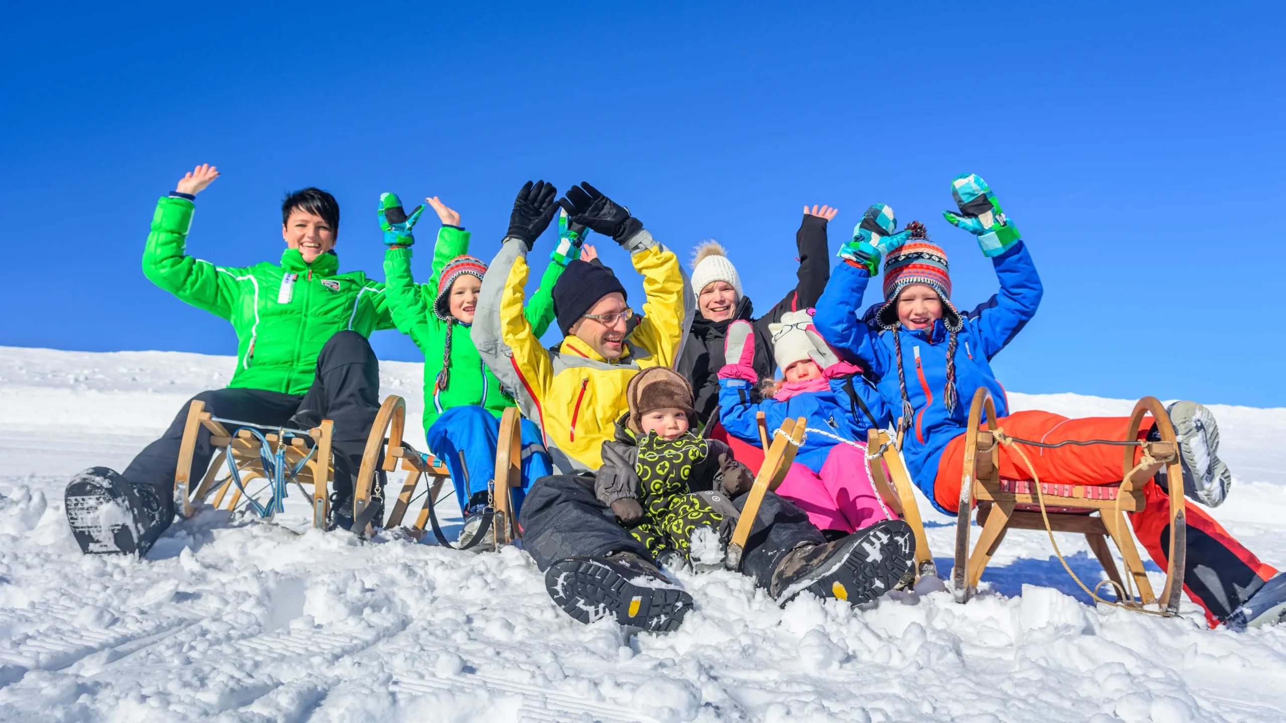 Several individuals sitting together on a sled, laughing and sliding down a snowy hill, dressed warmly for the cold weather.