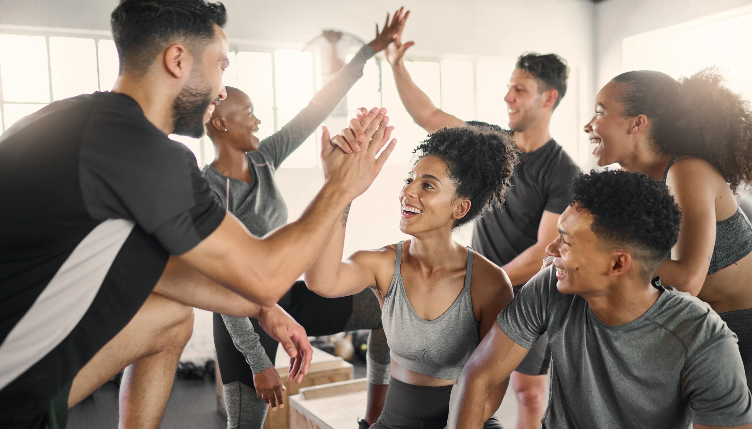 A group of six people in a gym enthusiastically giving high fives, celebrating their commitment to their health and wellness goals.