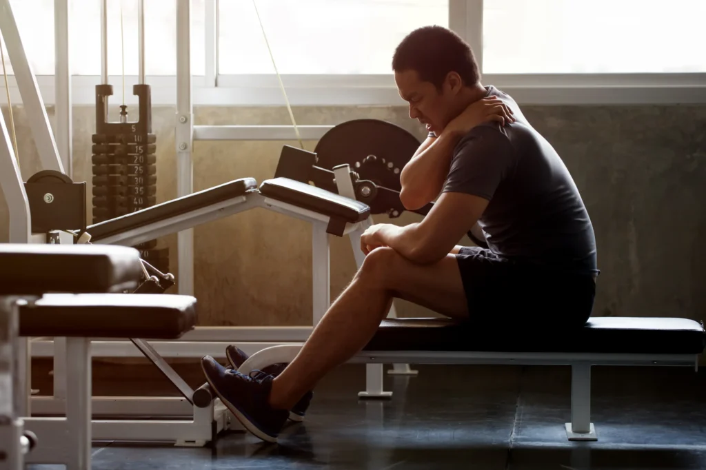 A man sitting on a workout bench grabbing his shoulder in pain