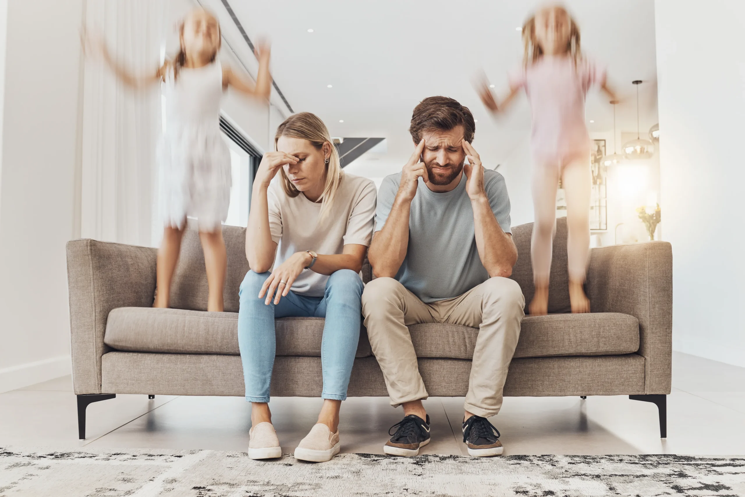 Parents in distress from children being hyper jumping on the couch while they may have a headache.