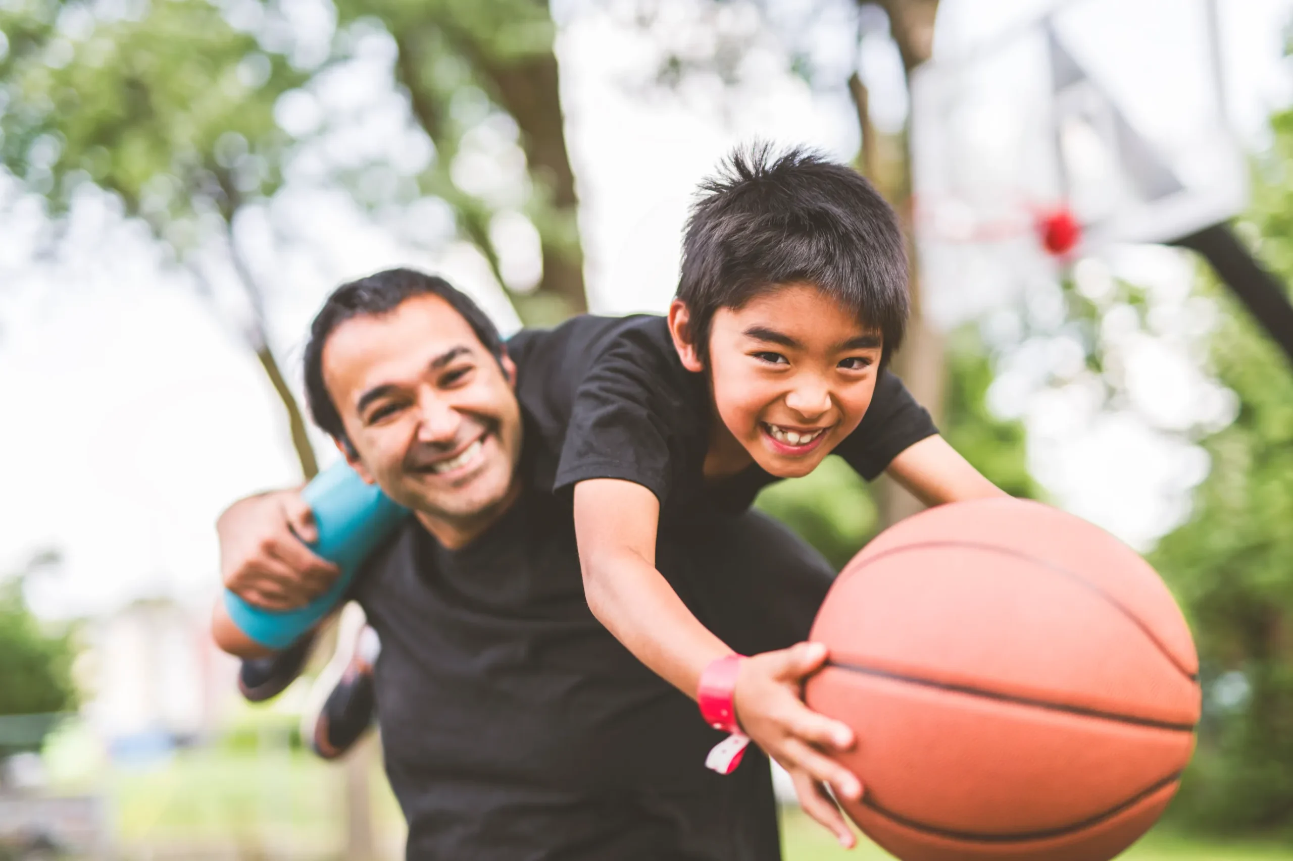 A man and a boy are holding a basketball, representing the joy of sports and the benefits of physical therapy for staying active.