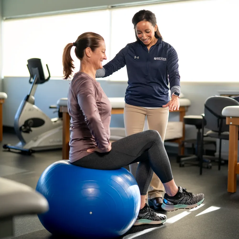 PT guiding patient on a yoga ball.