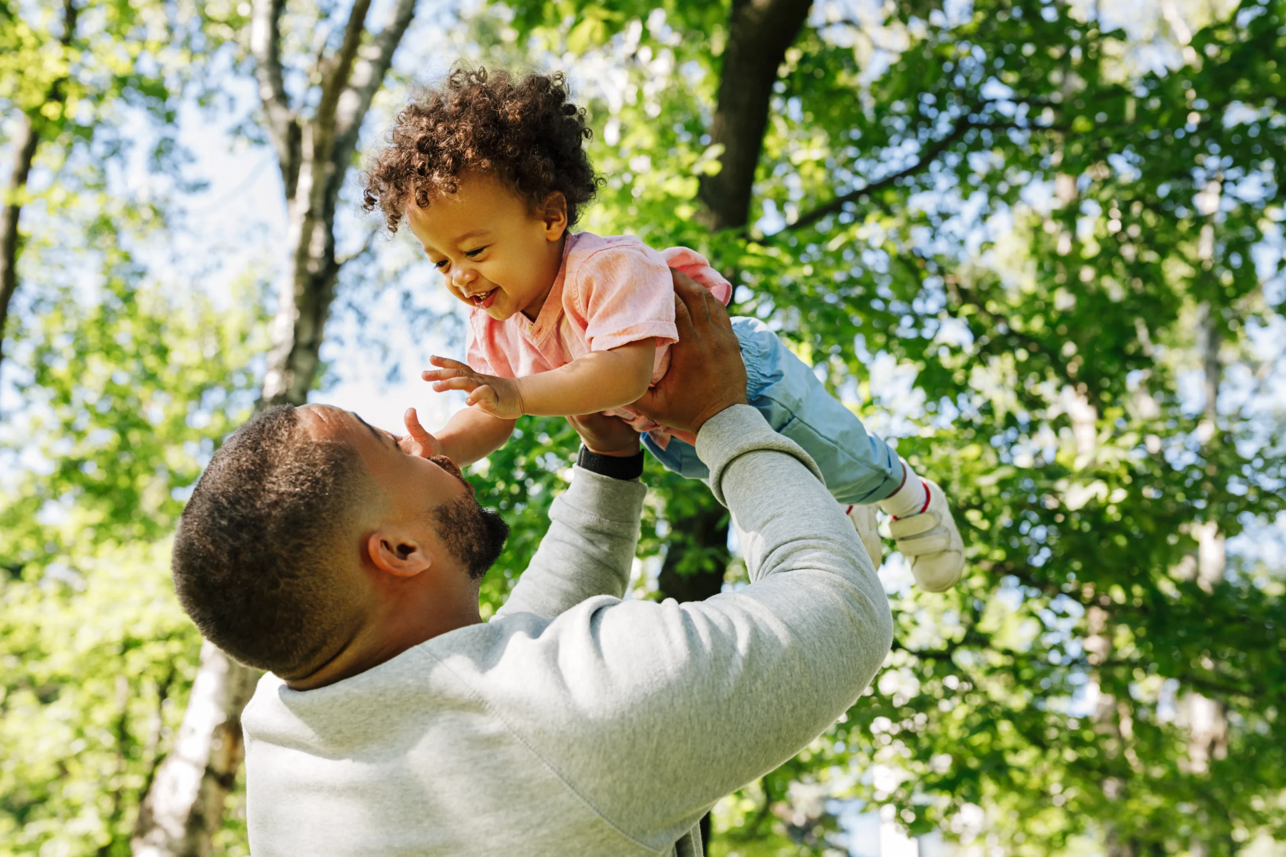 Father carrying child and playing outside laughing.