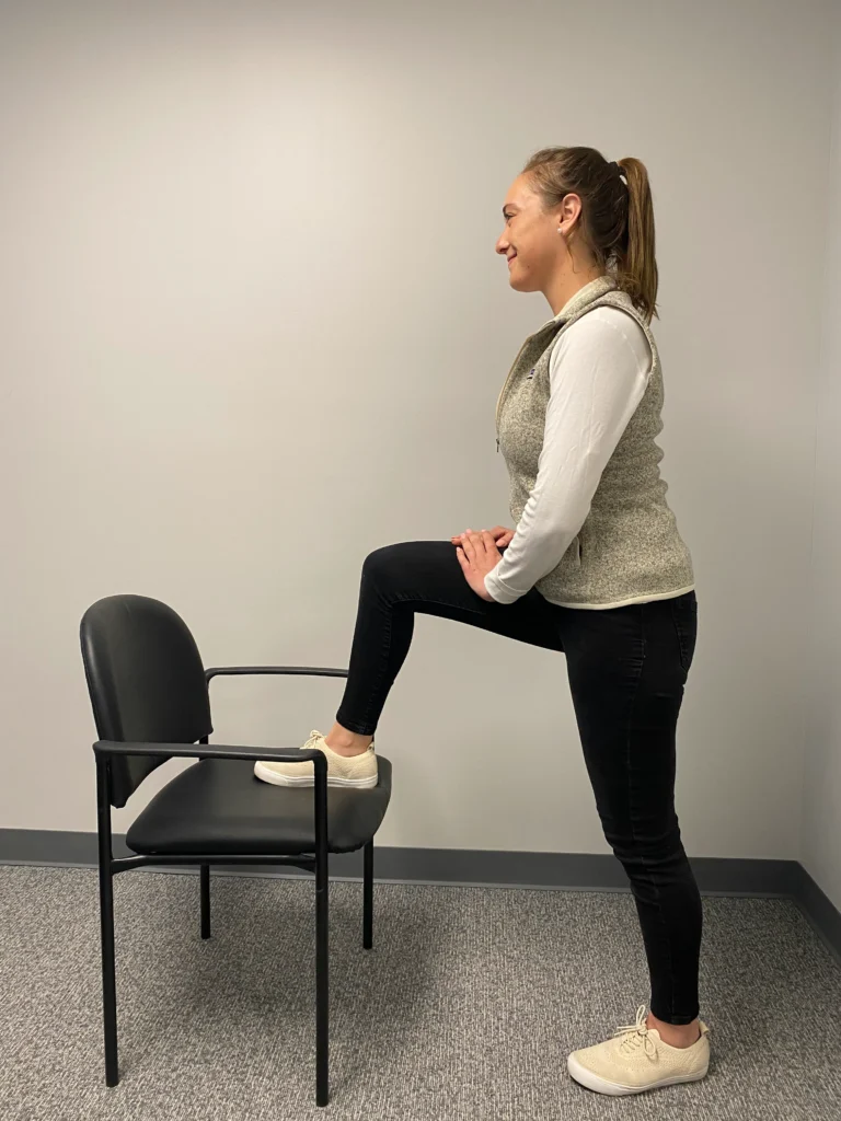Side view of a women demonstrating Hip Flexor Stretch on her right leg with a char.