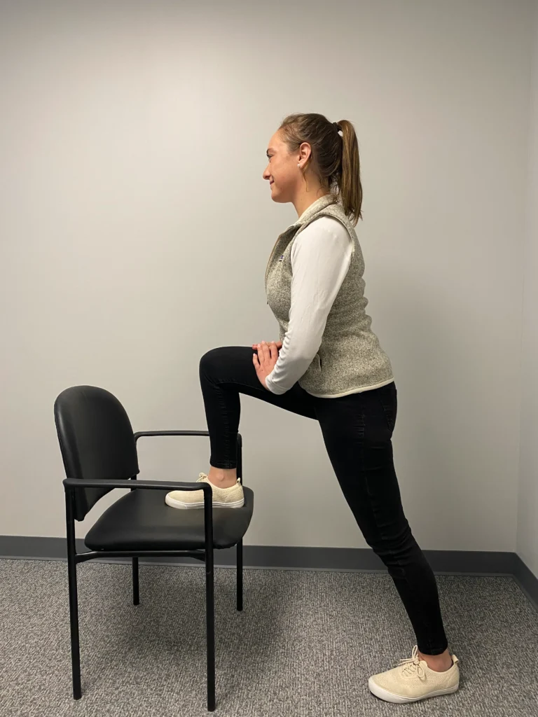 Side view of a women demonstrating Hip Flexor Stretch on her right leg with a char.