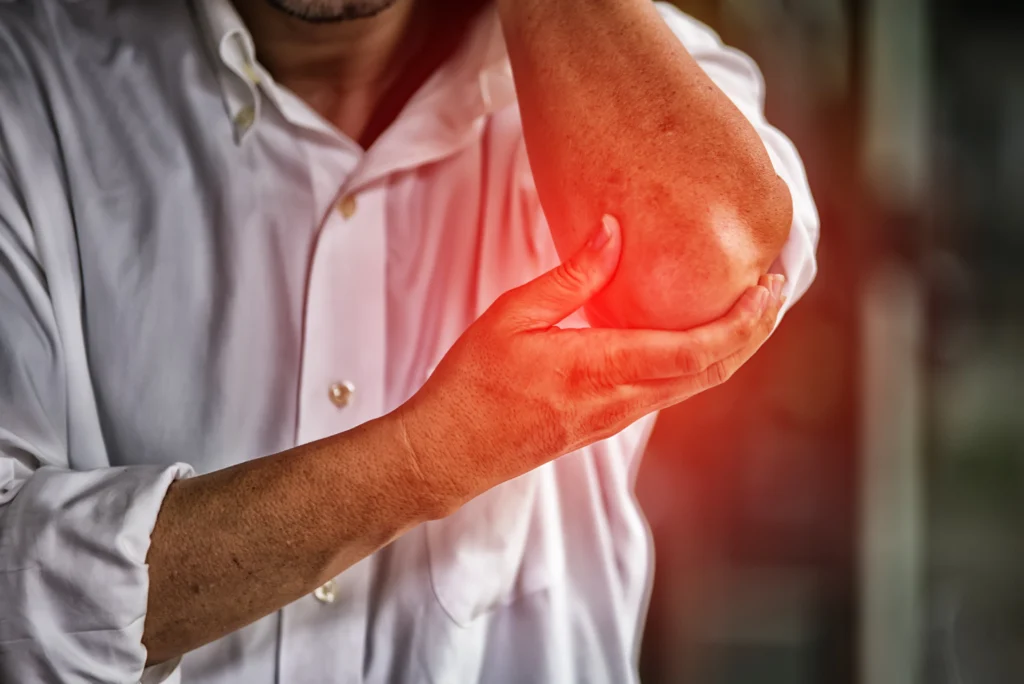 A man clutches his elbow in discomfort, clearly indicating he is dealing with elbow pain.