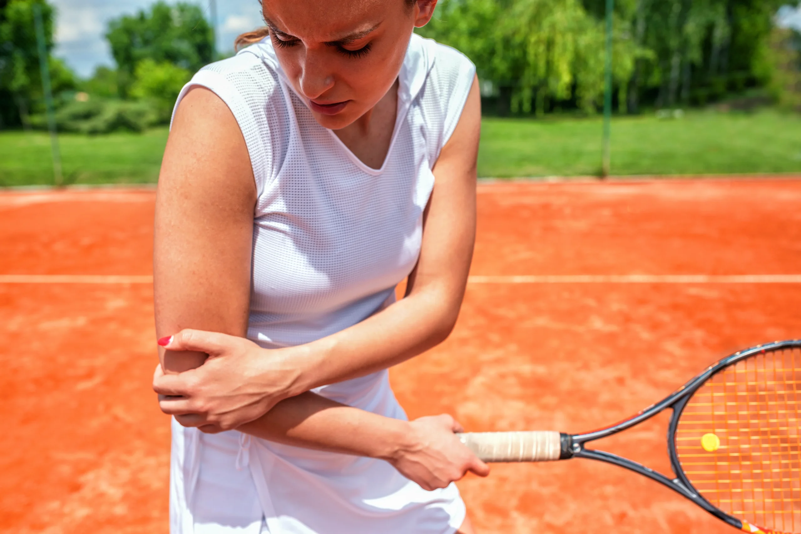 Woman gripping her elbow in pain while playing tennis, illustrating tennis elbow pain treatment and management.