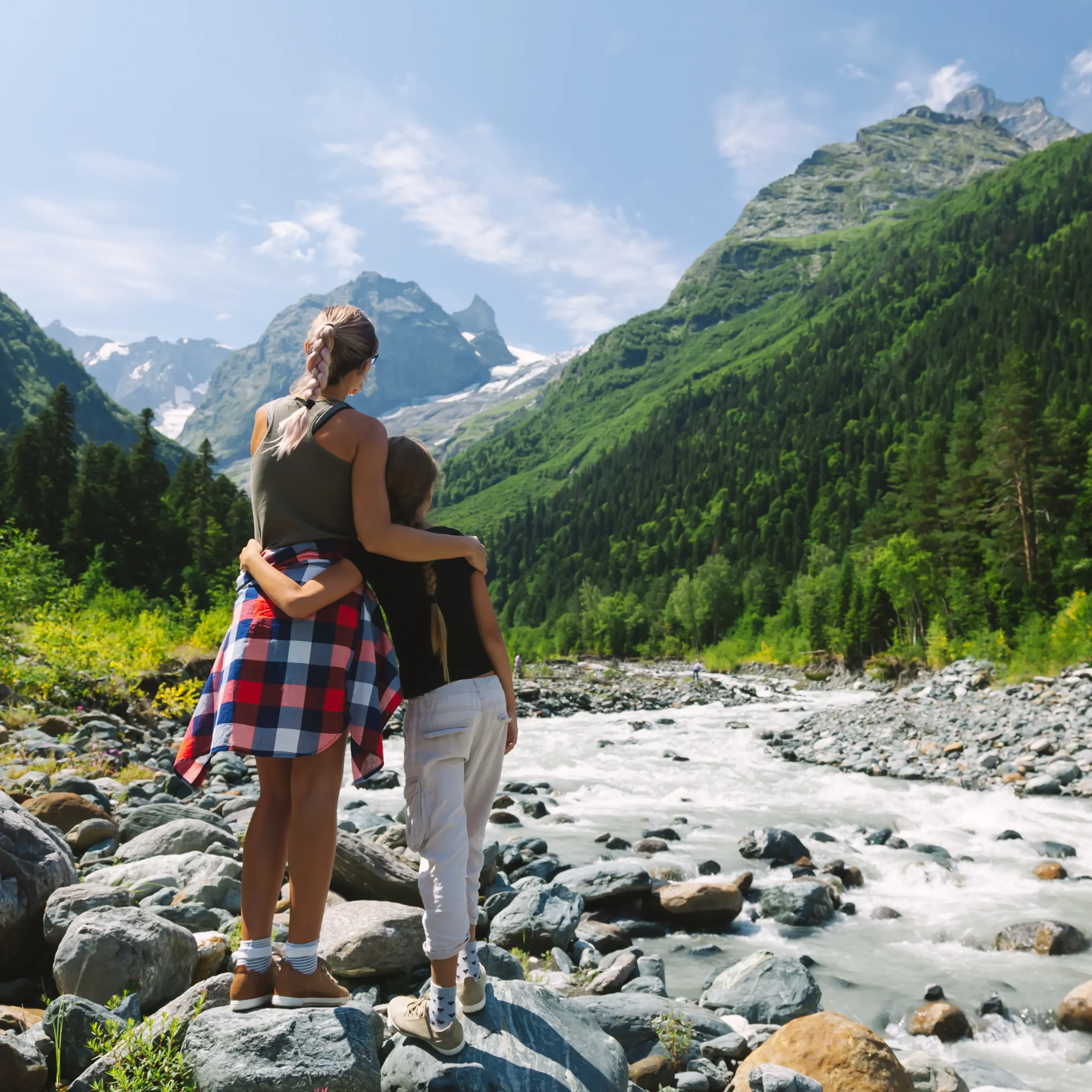 Two women stand on rocks, gazing at a river and mountains, featured in the Off-Season Survival Guide.